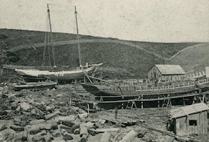 Shipyard with two boats under construction with small buildings nearby