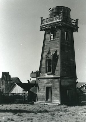 A large water tower featuring decorative woodwork with buildings in the background