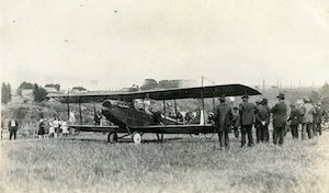 An early-model airplane in a field surrounded by onlookers
