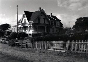 A large Victorian-style house with a flagpole in front of it and a fence along the property