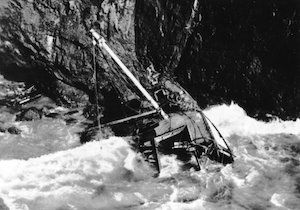A shipwreck in the water pushed against high rocks