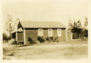 A small wooden schoolhouse with trees in the background