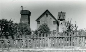 A church building and water tower behind trees and a fence