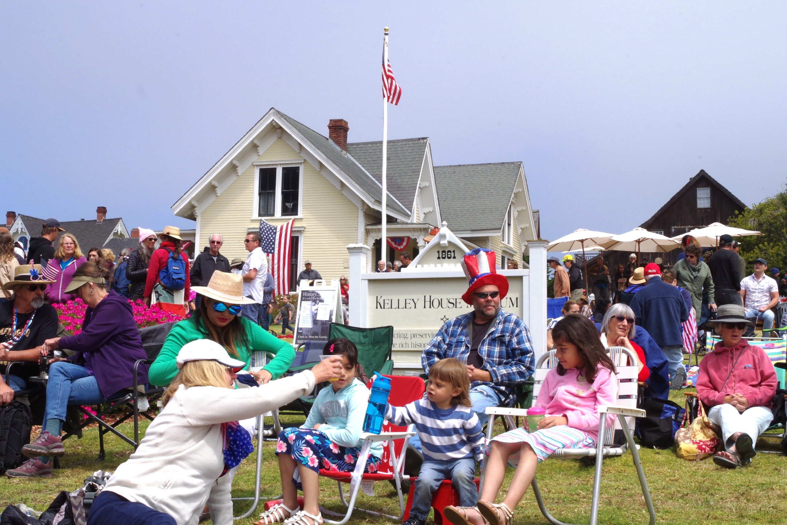 People sitting on a lawn with the Kelley House Museum and sign behind them