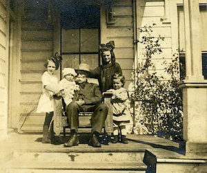 Elderly man seated on porch, surrounded by 4 children