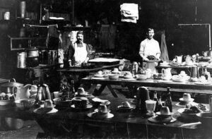 Two men standing in a cookhouse behind tables with dishes