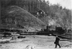 Man on beach with boat behind him. 4 water tanks on bluff in background.