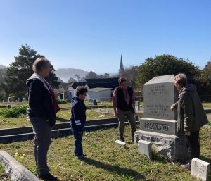 Four people look at a large tombstone in a cemetery