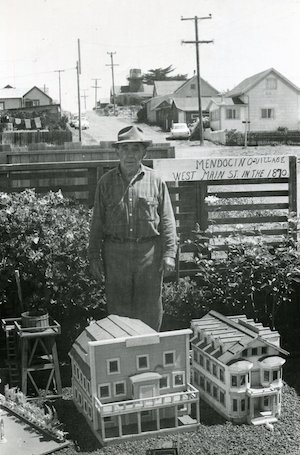 Man in hat standing behind miniature houses