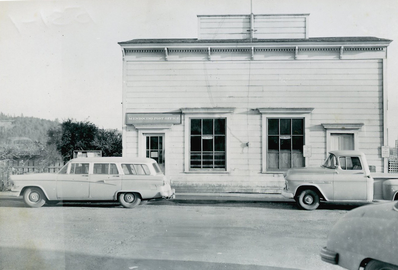 Station wagon and truck parked in front of a building. A sign on the building reads “Mendocino Post Office.”