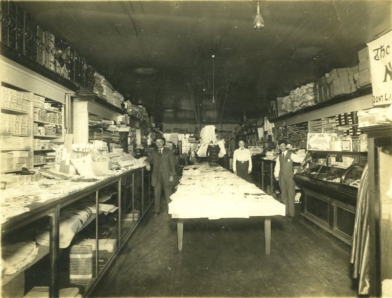 Two men and a woman stand in the aisles of an old store.