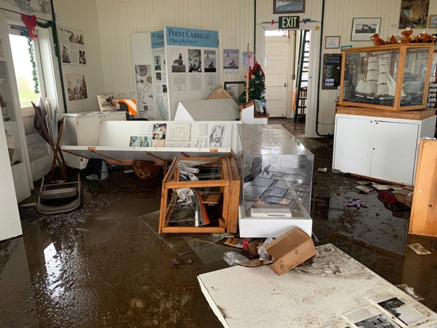 Inside a water-damaged gift shop. Display cases and merchandise are scattered on the soaked floor.