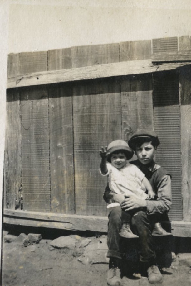 Two children sitting in front of a board fence