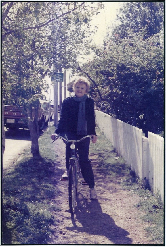 Woman straddling bicycle dressed in a jacket, long scarf, and sneakers