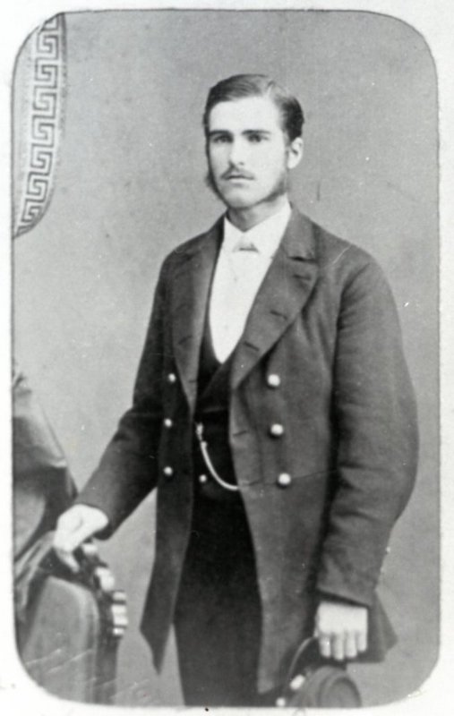 Studio portrait of a young man, posed with a chair and holding a hat.