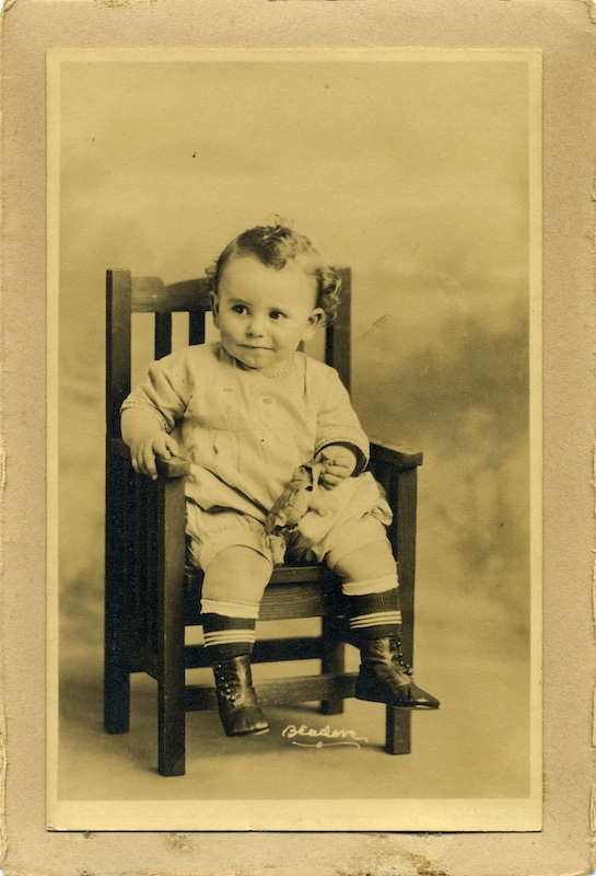 Small child sitting in a chair, holding a toy.