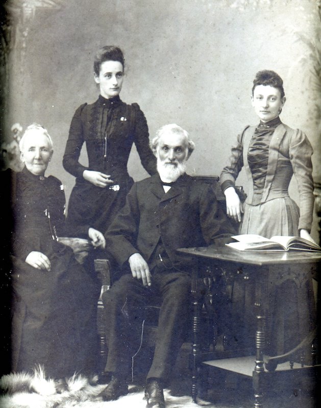 Elderly couple seated in foreground, two adult women stand behind them.