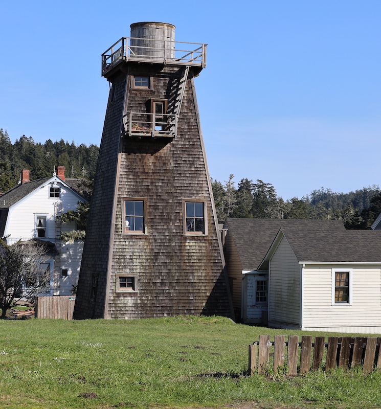 Water Tower with outbuildings. Two-story house in the background.