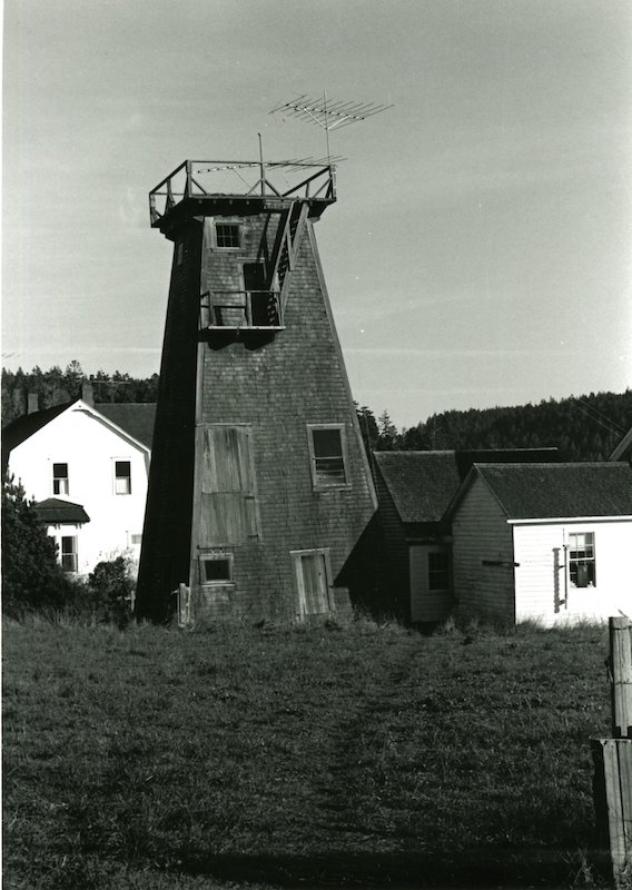 Water Tower with outbuildings. Two-story house in the background.