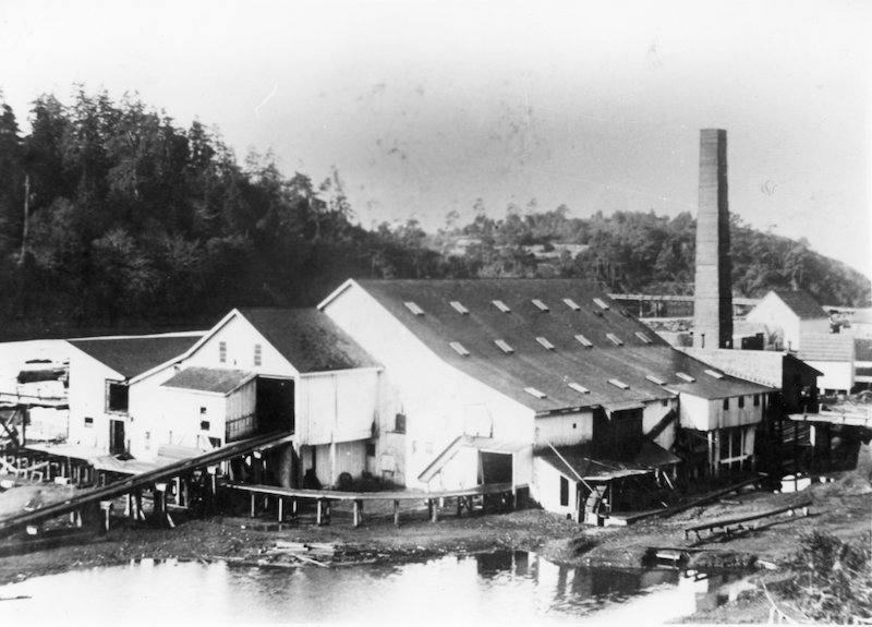 Saw mill in foreground and tall brick chimney in background