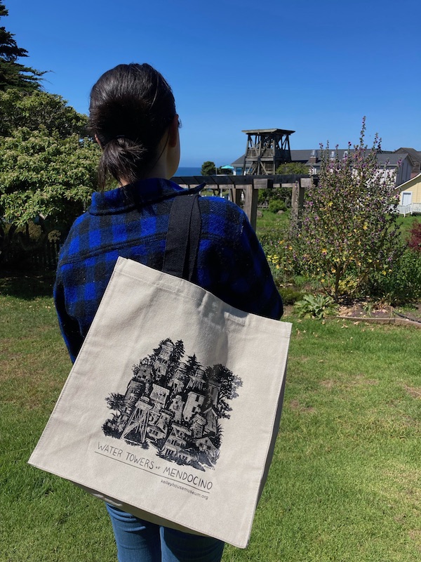 Woman carrying tote bag with water tower screen print looks towards a water tower