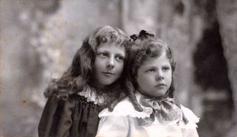Boy with long hair leans toward a girl with a ribbon in her hair