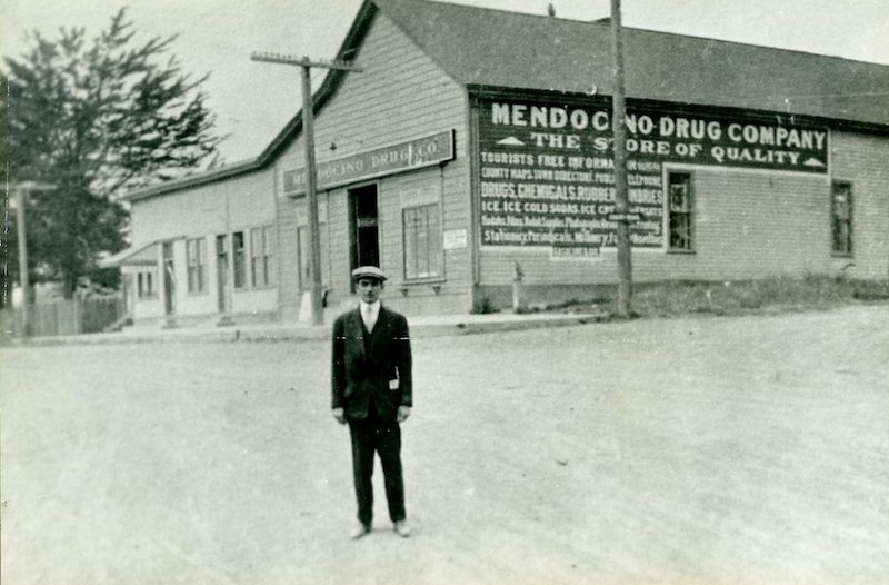 Intersection of two dirt roads. Man poses in center of intersection. Commercial building in background.
