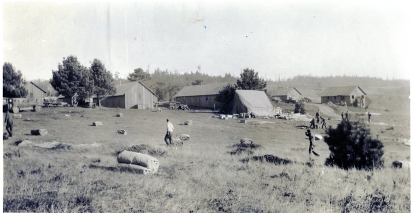 Black and White photo of a camp with tents and buildings in a field