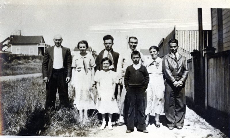 Parents and 6 children standing next to a home
