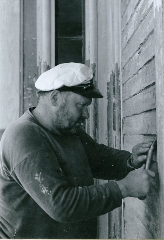 Man in cap scraping paint from exterior siding