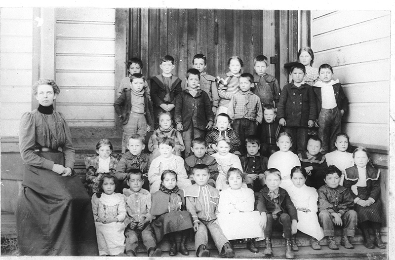 Children and teachers posed on schoolhouse steps