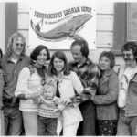 several adults and child posing in front of Mendocino Whale War sign