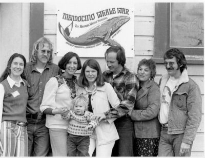 several adults and child posing in front of Mendocino Whale War sign