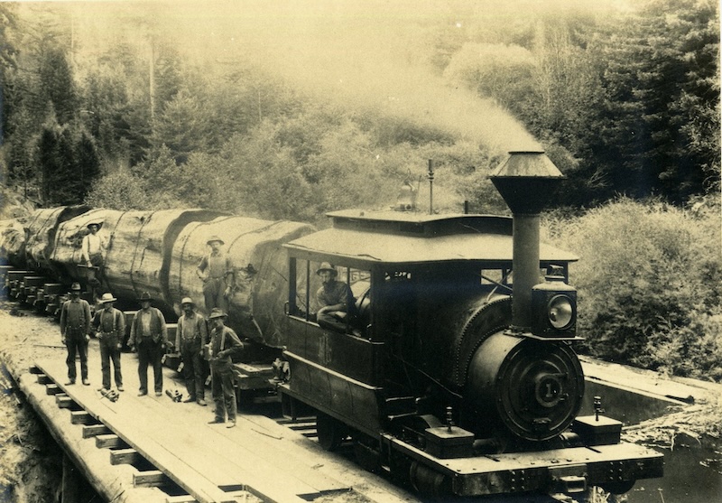Locomotive Engine and men posing with four enormous redwood log sections on rail cars.