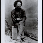 man in hat sitting on stump in black white photo