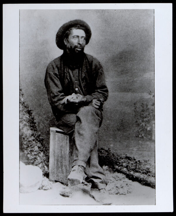 man in hat sitting on stump in black white photo