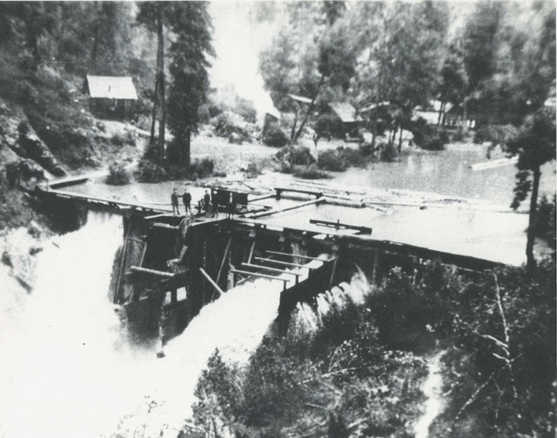 Men standing on top of a wooden dam, with water pouring out of the gate
