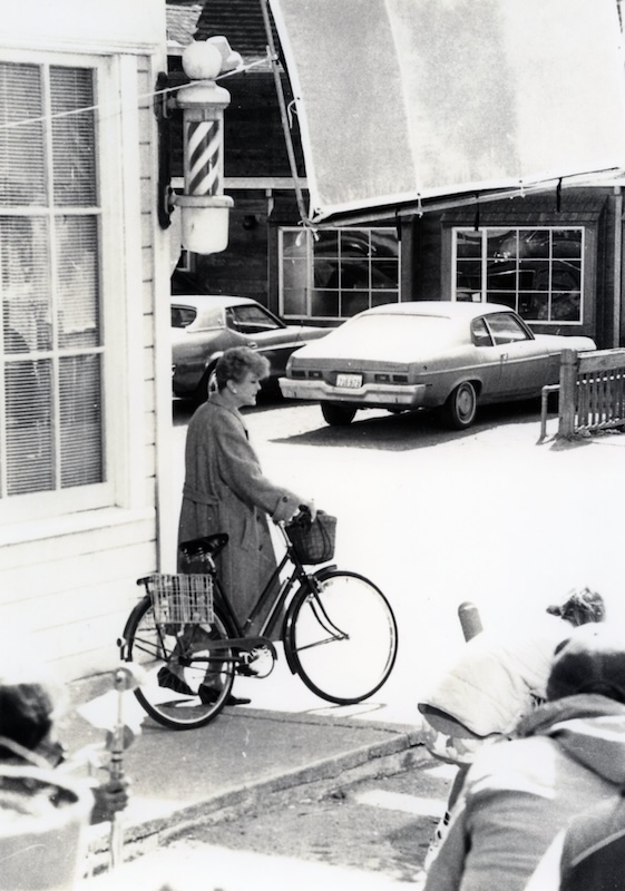 Actress wheels bicycle with film crew in foreground