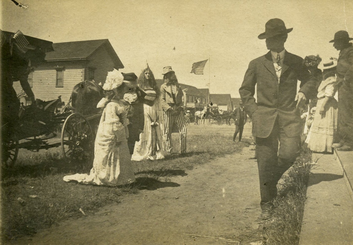 Two costumed people, a woman dressed as the Goddess of Liberty (Columbia), and a man dressed as Uncle Sam, mingle with carriages and the crowd gathered on the steps. A man in a suit and hat walks by in the foreground