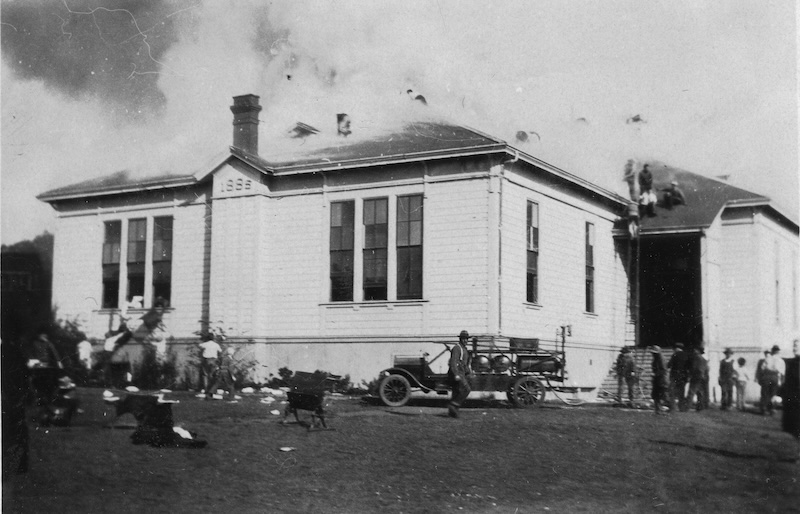 Historical School Building with chimney. Smoke surrounds roof, old-fashioned vehicle in front