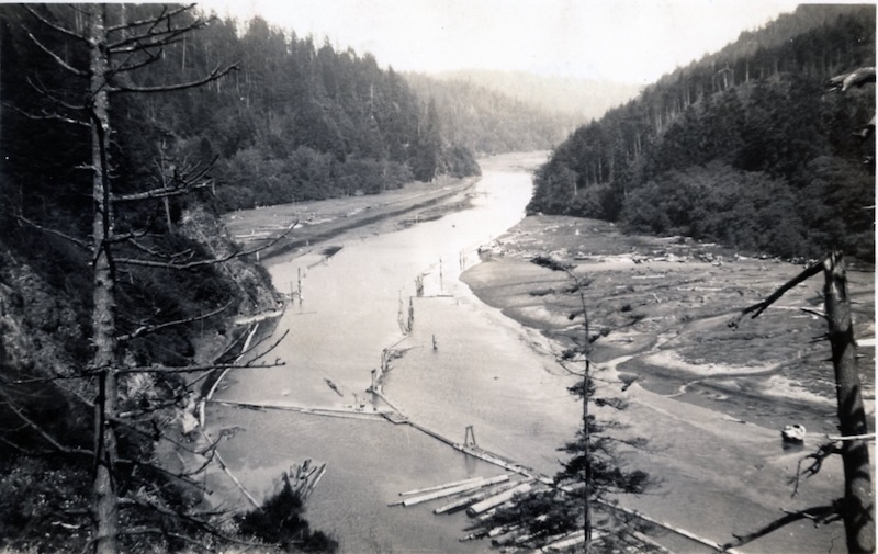 Scene looking upriver. In the foreground is an enclosed area with large floating logs.