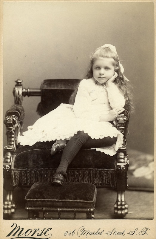 Little girl in a frilly white dress poses in a chair