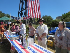 Tables with people behind them selling food and drinks and a water tower draped in an American flag in the background
