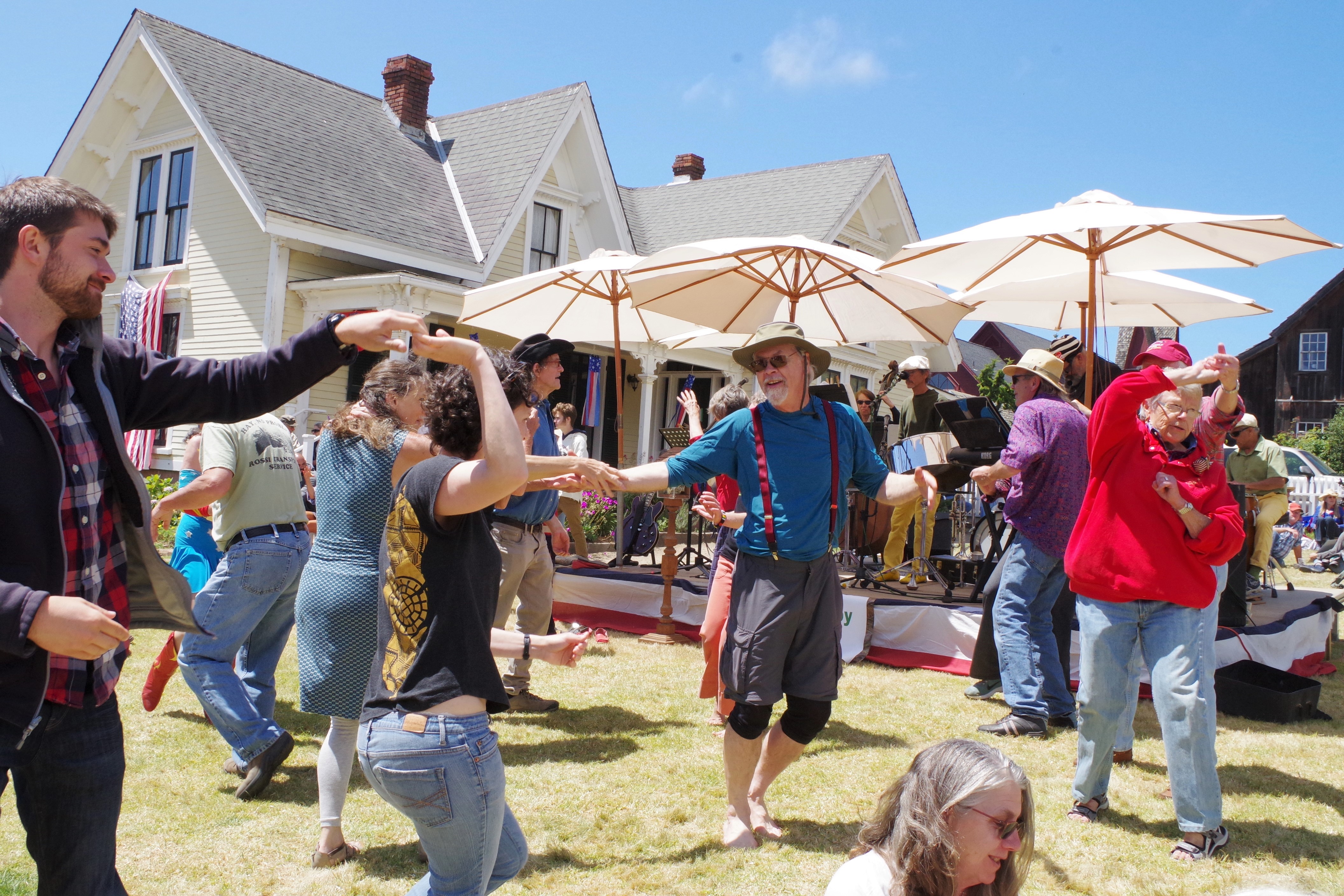 People dancing in front of a house with umbrellas and tables behind them
