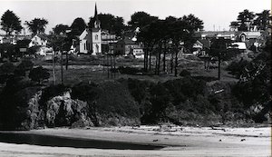 Grassy hills topped with buildings and trees sloping down to a beach