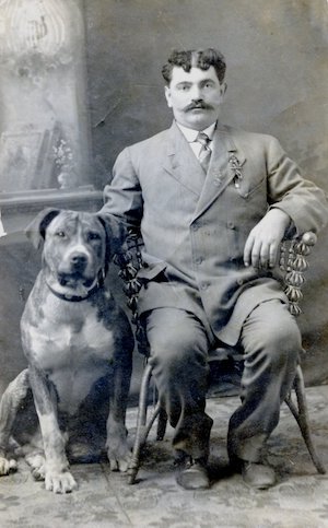 Portrait of a man with a mustache wearing a suit seated beside a large dog