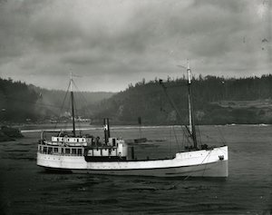 A large steam ship on the water with wooded hills in the background