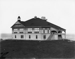 A large building on a hill with the ocean behind it