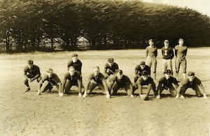 Young men in football uniforms posing on a field with trees behind them