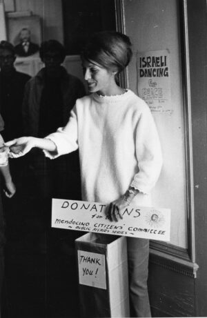 A woman with a box saying "Thank You!" on it holding a sign asking for donations